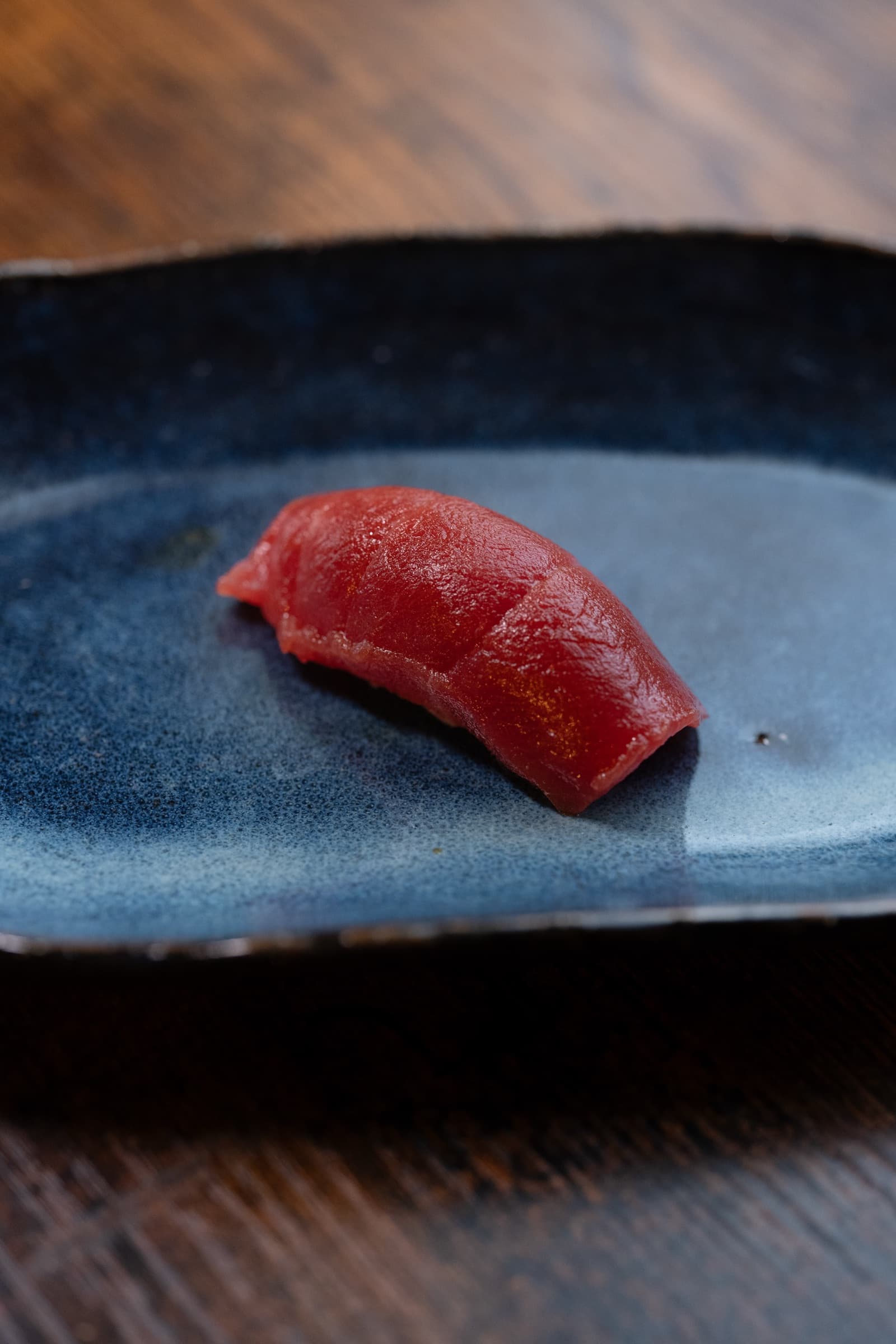 A single piece of tuna nigiri sushi on a dark ceramic plate